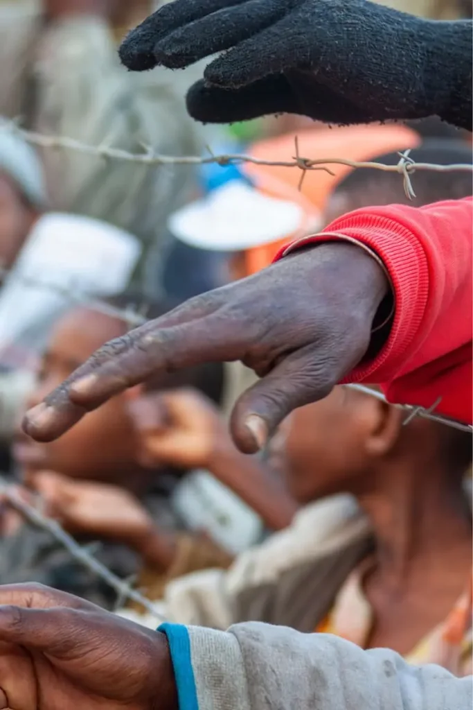 hands protruding through a wire fence
